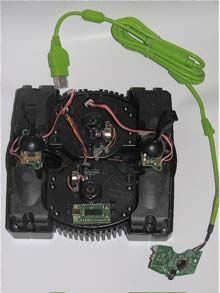 An opened Gametrak base with its two tether sensor assemblies and wiring, and a small green circuit board on a green USB cable.